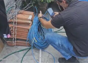 Empresa de Internet Interditada por Uso de Cabos Furtados em Duque de Caxias" Uma operação da Polícia Civil resultou na interdição de uma empresa de internet em Duque de Caxias, na Baixada Fluminense, por envolvimento no uso de cabos furtados em seus serviços. Durante a ação, agentes flagraram dois funcionários, identificados pelos adesivos da empresa em seus carros, realizando um serviço no bairro Taquara sem a documentação adequada para os cabos utilizados. Os funcionários não possuíam comprovação para a utilização dos cabos, e ao serem abordados, indicaram o responsável pela empresa. As investigações levaram os policiais até a sede da companhia, onde mais um funcionário foi encontrado. No local, foram descobertos diversos cabos que traziam a identificação de duas empresas de telefonia. A operação culminou na prisão dos envolvidos, que foram autuados por receptação qualificada, reforçando a atuação enérgica da polícia na repressão de atividades ilícitas